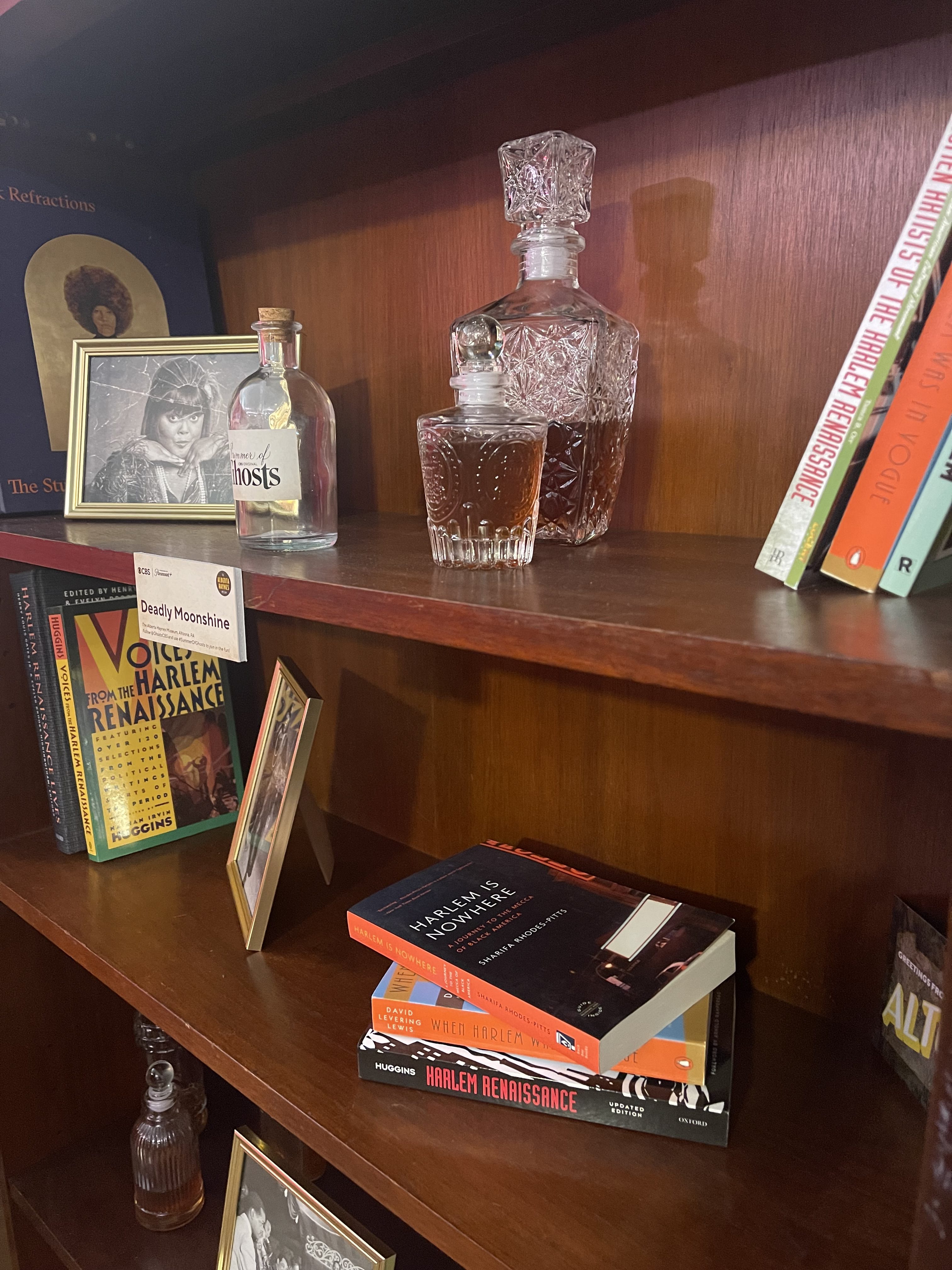 Museum shelf displaying Alberta photographs, Harlem history books and moonshine decanters
