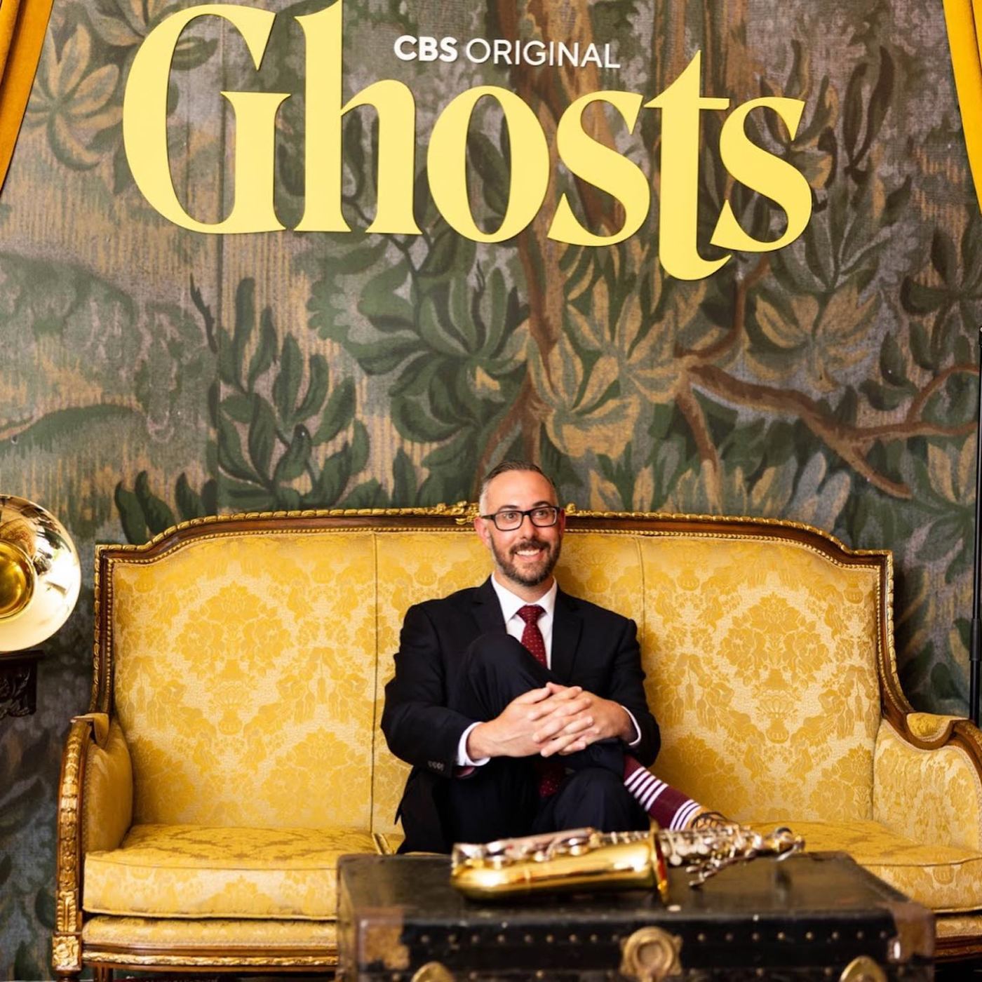 Guest on the gold damask settee beneath the Ghosts tapestry backdrop with brass horn