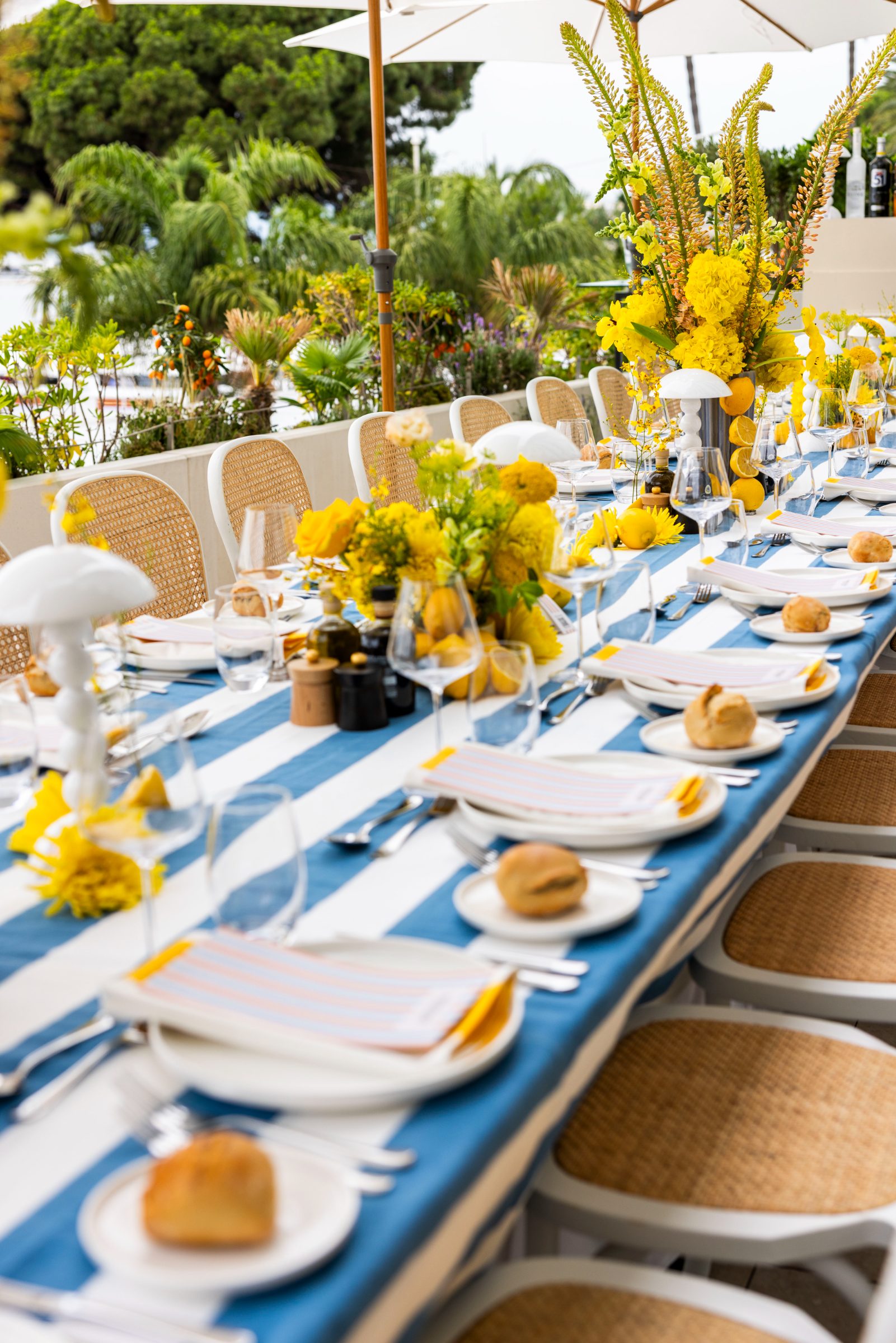 A long lunch table set with striped linens and yellow florals on the JW Marriott terrace