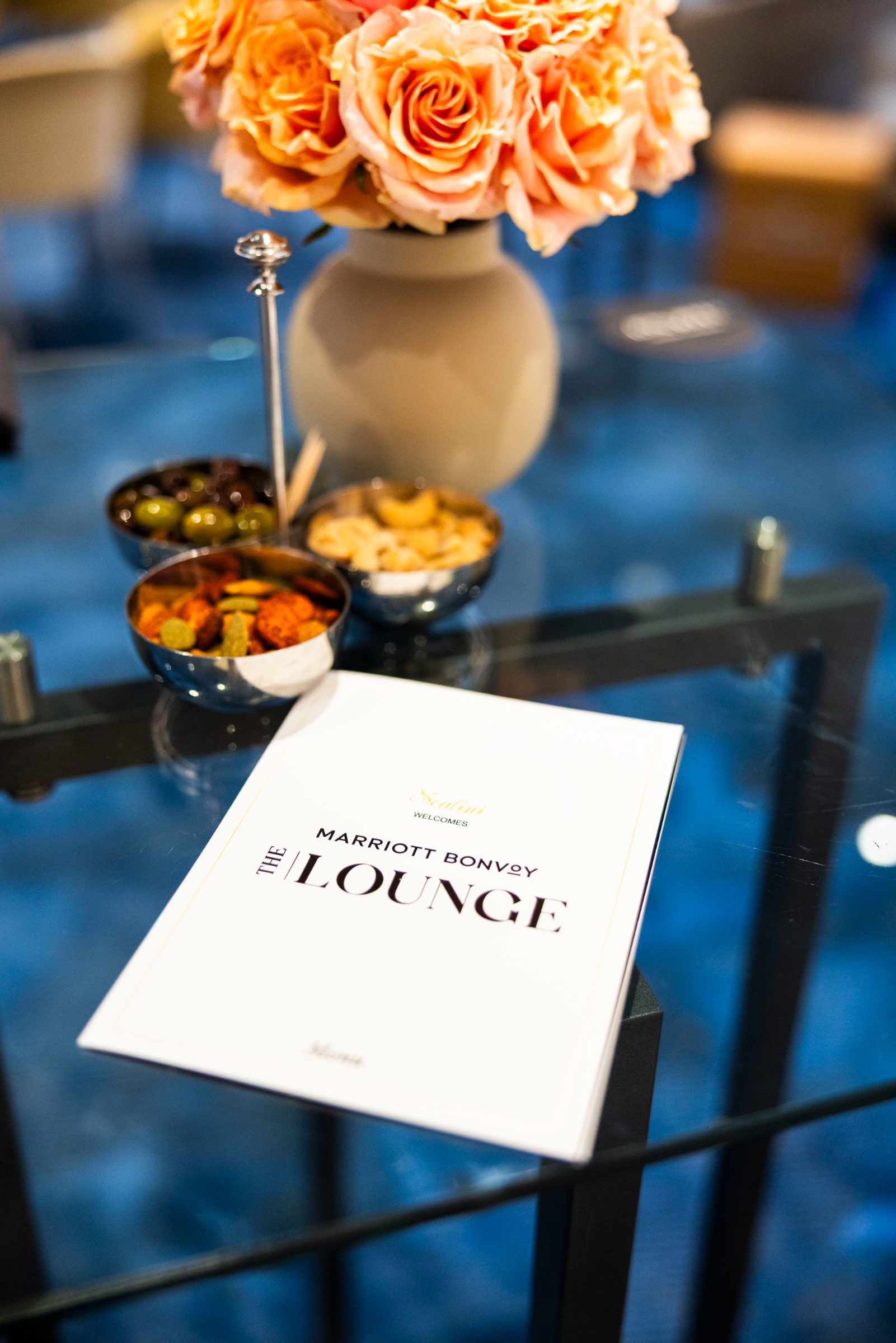 The Lounge menu beside roses and snacks on a glass table
