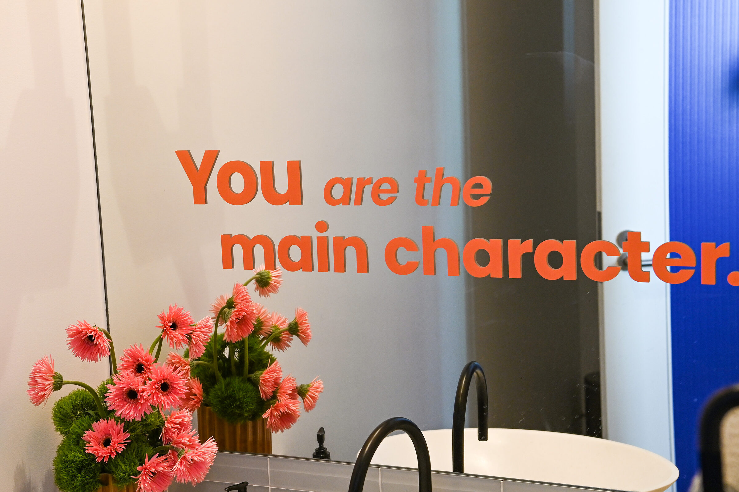 'You are the main character' graphic above a floral arrangement in the powder room