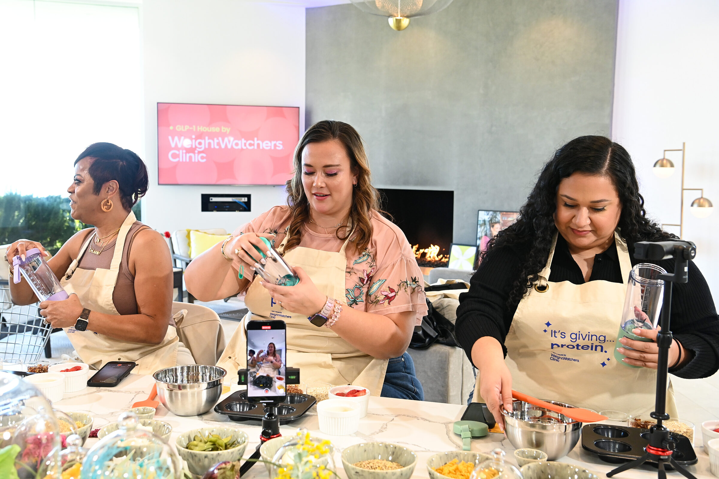 Aproned creators filming themselves preparing a recipe at the kitchen baking stations