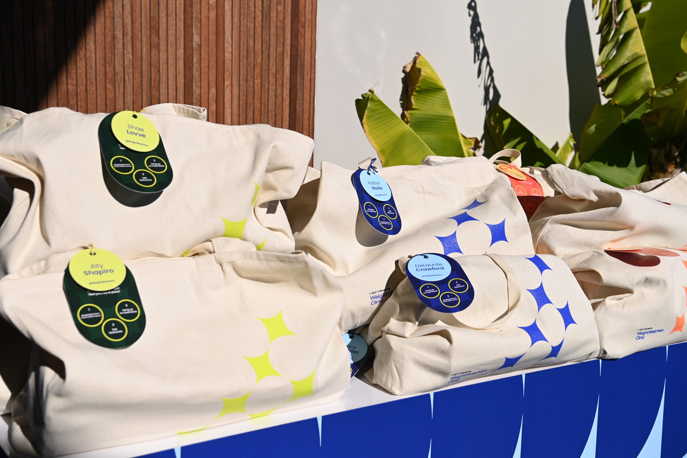 Branded canvas tote content kits stacked on a blurple plinth